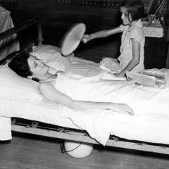 A little girl in 1938 fans her sick mother, who works in a box factory. Huey Long greatly expanded access by the rural poor to professional healthcare.